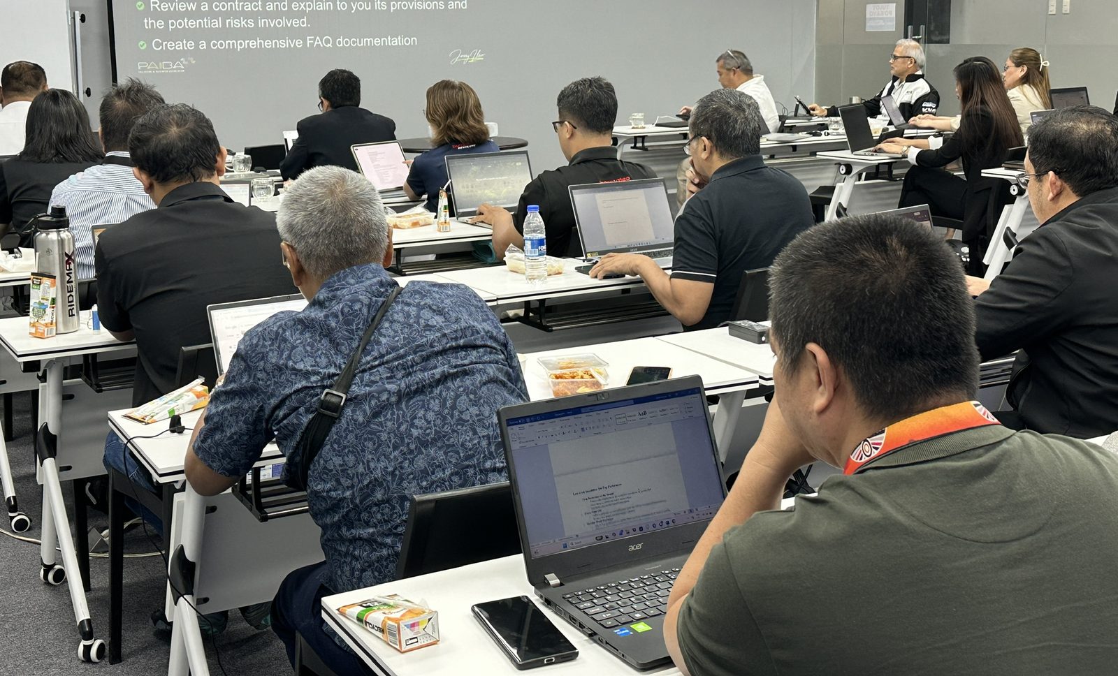 Participants heads-down on laptops doing applied AI exercises — reviewing contracts and building FAQ documents