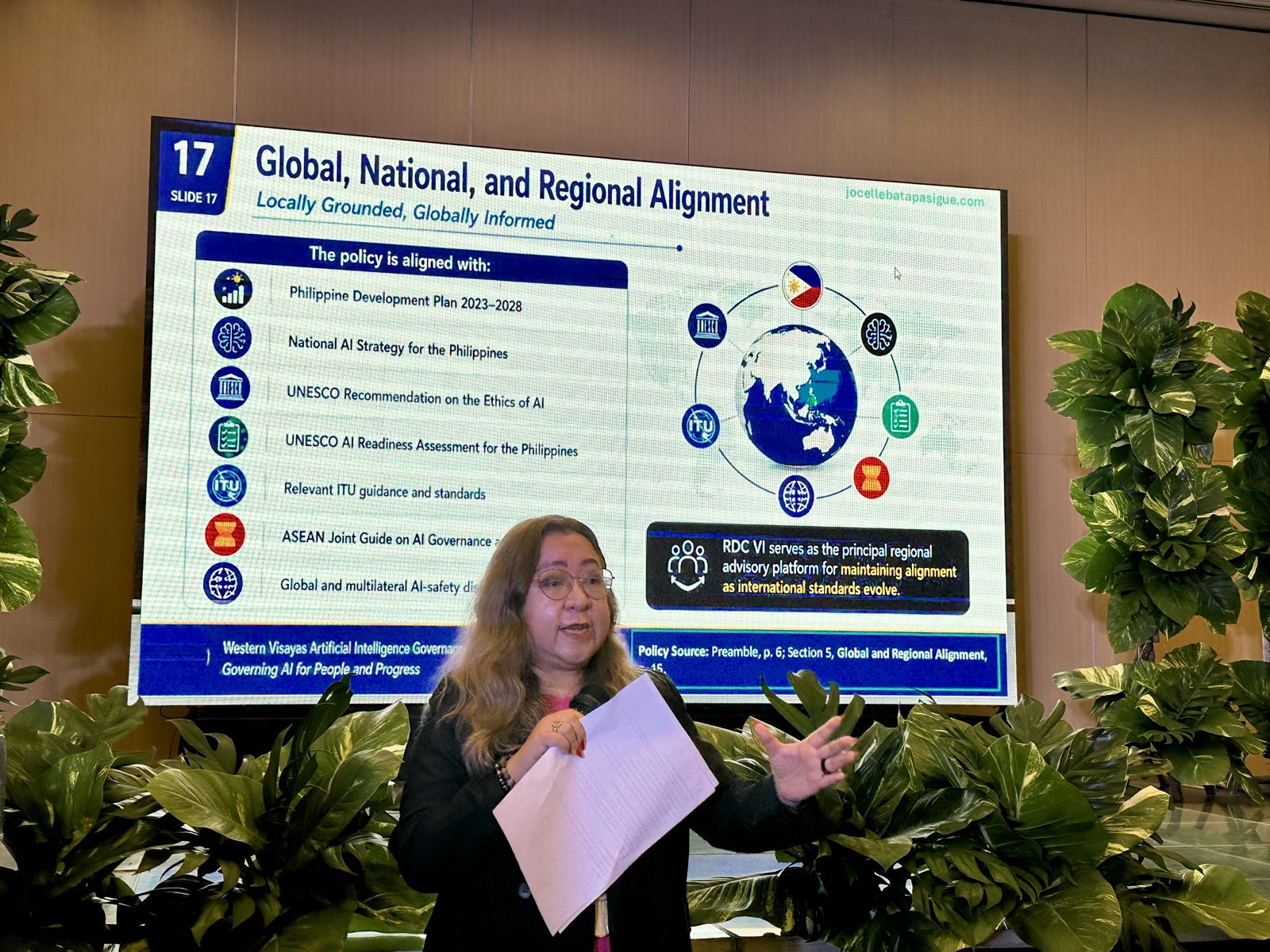 Atty. Batapa-Sigue beside a slide mapping the Western Visayas policy's alignment with national plans and UNESCO, ITU, and ASEAN frameworks